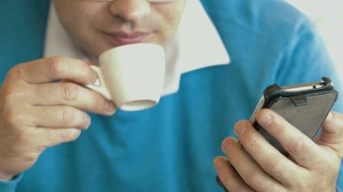 Adult Using Phone and Writing While Drinking Coffee