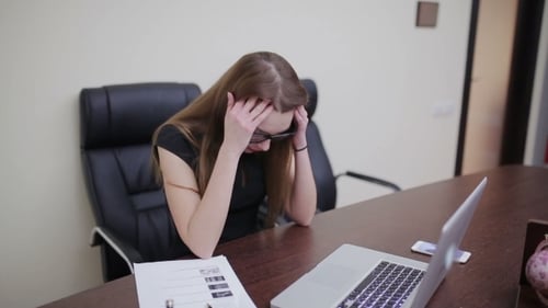 Stressed Woman Rubbing Temples at Desk in Office