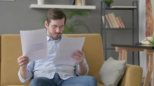 Man Reading Documents on Couch is Concerned