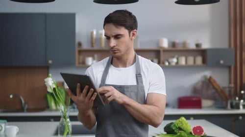 Man in Apron Using Tablet in Kitchen