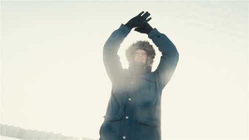Man with Fur Hoody Raises Arms in Winter Snow