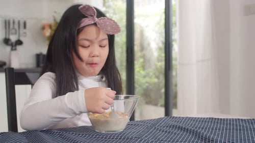 Girl Enjoys Cereal at Kitchen Table in Morning