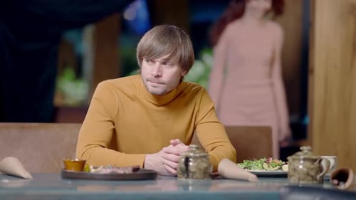 Portrait of Worried Young Caucasian Man Checking Time Sitting in Restaurant As Woman Entering Cafe