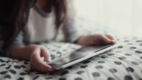 Young Adult Using Tablet on Bed At Home