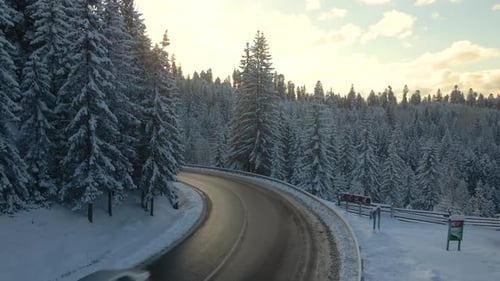 Aerial view of winter landscape with snow covered mountain hills and winding forest road in morning.