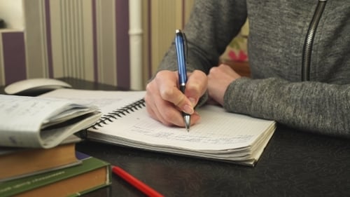 Young Adult Writing in Notebook with Blue Pen