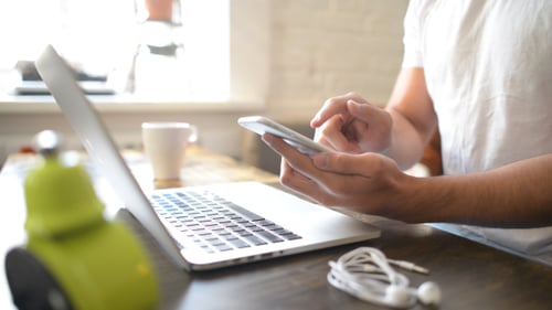 Young Adult Using Cellphone at Table with Laptop