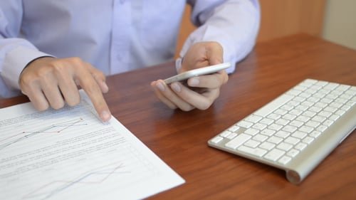 Adult Using Phone While Viewing Charts At Desk