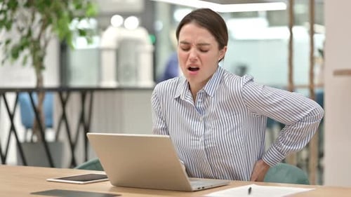 Tired Young Woman with Laptop Having Back Pain in Office