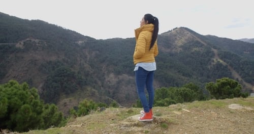 Mujer en abrigo amarillo cerca del valle de la montaña