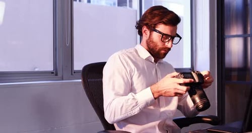 Man Examining Camera at Desk in Office