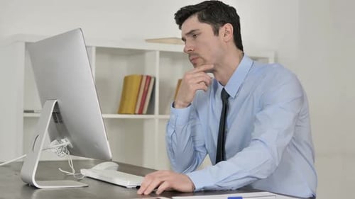 Man Thinking at Computer in Bright Office