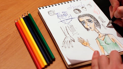 Hands Drawing Sketch in Notebook with Pencils