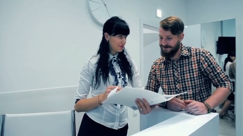 Man and Woman Discussing Paperwork at Reception Desk