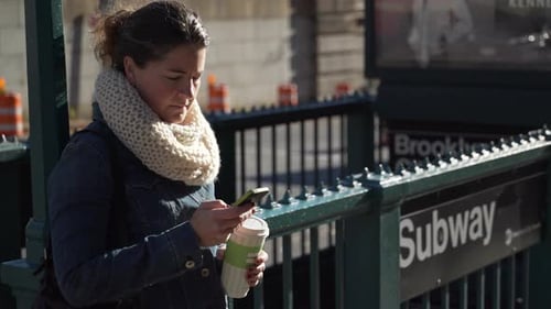 A Young Woman Is Looking At Her Phone Near A Subway Station 1