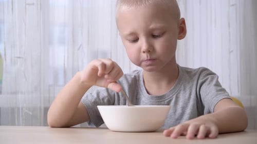 Young Boy Eating Cereal at Table in Bright Light