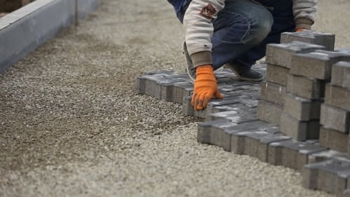 Construction Worker Laying Gray Bricks on Urban Street