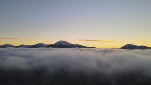 Aerial View of Vibrant Sunrise Over White Dense Clouds with Distant Dark Mountains on Horizon