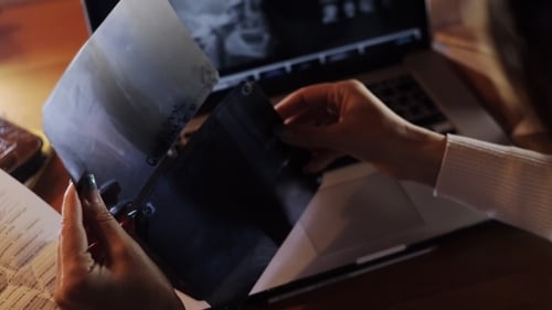 Woman Examines X-Ray at Desk With Laptop