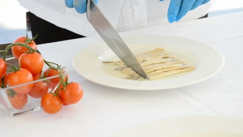 Chef Cuts Anchovies with Knife on White Plate