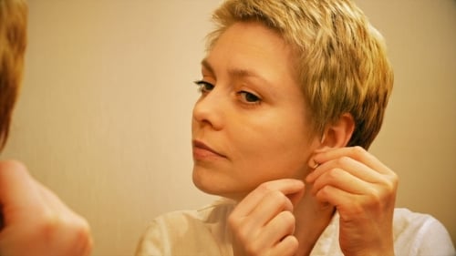 Woman Putting on Earrings in Front of Mirror