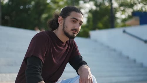 Portrait of Young Attractive Arab Man Sitting on the Stairs in Park at Sunset