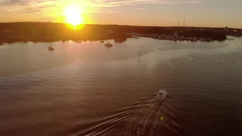 Vista aérea de una lancha motora que entra en el puerto de una hermosa ciudad pequeña en un río tranquilo bajo un colorido s