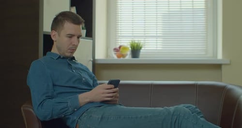 Young Adult Uses Phone Relaxing Indoors