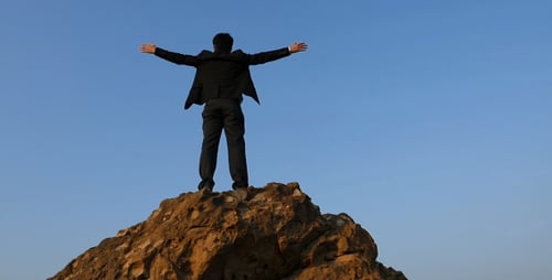 Man in Suit Stands on Rocky Peak with Arms Out
