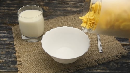 Pouring Cornflakes into Bowl for Breakfast with Milk