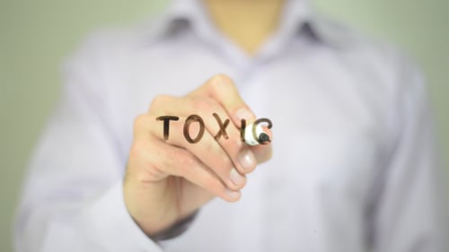 Hand Writes the Word Toxic on Clear Surface