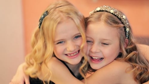 Two Blonde Girls Smiling and Embracing Indoors