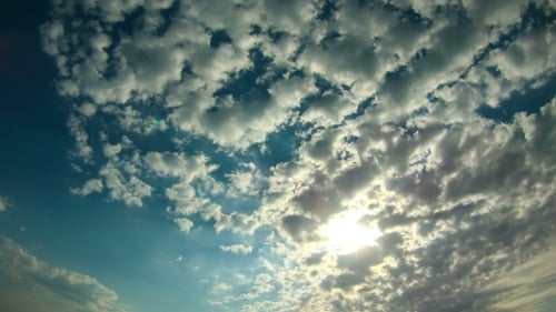 Wolken bewegen sich am Himmel, die Sonne scheint hell hinter den Wolken.