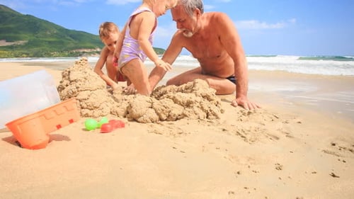 Niños del abuelo construyen un castillo de arena en la playa con Wave Surf