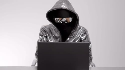 Masked Person Typing on Laptop in White Room
