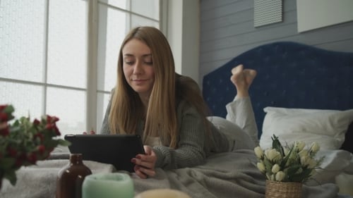 Woman Relaxes on Bed with Tablet Device