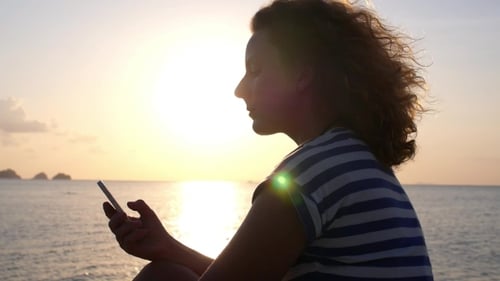Young Woman Using Smart Phone At Sea Sunset