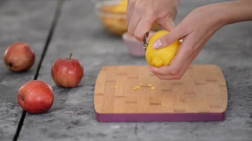 Woman Zests Lemon on Wood Cutting Board