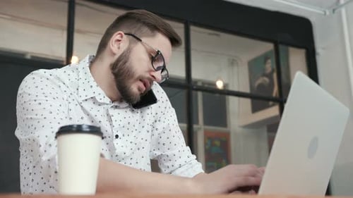 Man in Office Talking at Phone and Type at Laptop