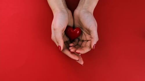 Hands Holding a Red Heart on Red Background