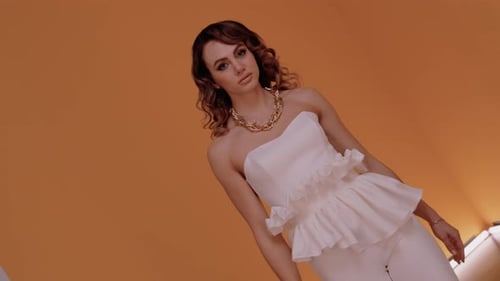 Elegant Woman Posing with Gold Necklace on Orange Backdrop