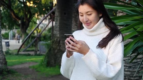 Young Woman Using Phone in Green City Park