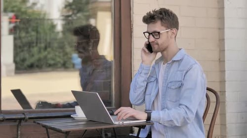 Man Working on Laptop and Talking on Phone
