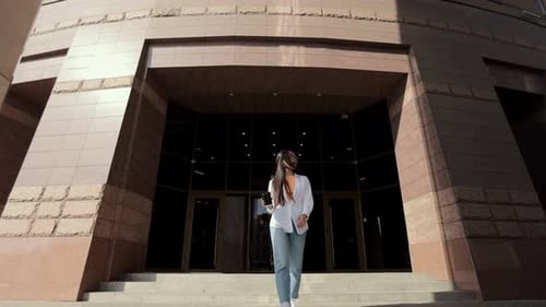 Serious Asian Woman Goes Near Modern Business Centre in the Urban Street Drinking Coffee