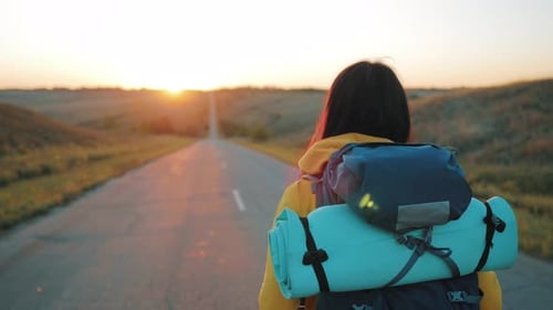 Woman Hiking Down Rural Road Towards Golden Sunrise