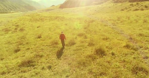 Flight Over Backpack Hiking Tourist Walking Across Green Mountain Field. Huge Rural Valley at Summer