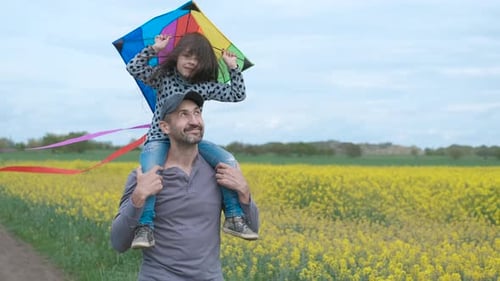 Father Carries Daughter with Kite Through Yellow Field