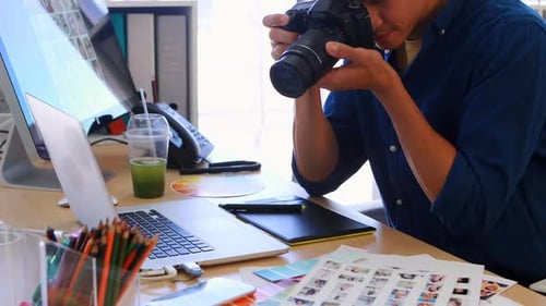Designer Taking Pictures of Photos at Desk