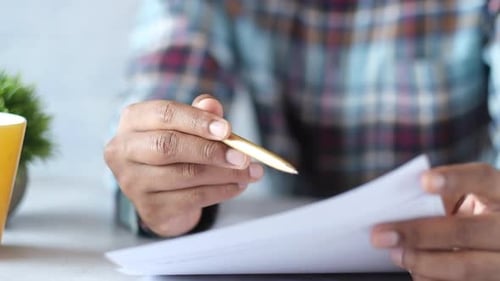 Mão de homem com caneta analisando gráfico financeiro em papel