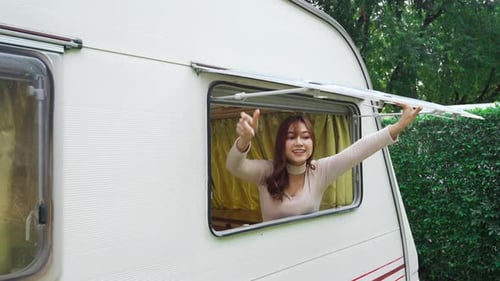 Woman Opens Camper Window in Green Setting